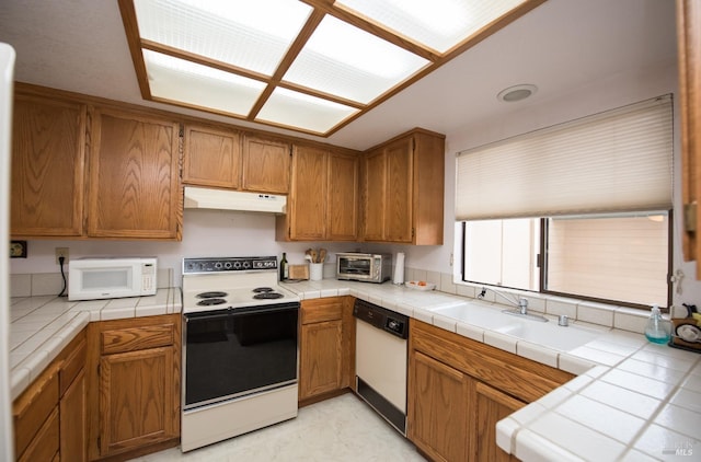 kitchen featuring tile countertops, brown cabinetry, under cabinet range hood, white appliances, and a toaster