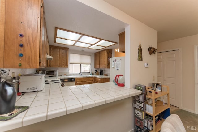 kitchen featuring white appliances, under cabinet range hood, a toaster, a peninsula, and brown cabinetry
