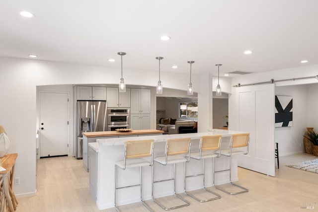 kitchen featuring gray cabinets, a kitchen island, decorative light fixtures, stainless steel appliances, and a barn door