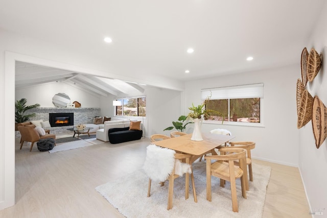 dining room with vaulted ceiling with beams, light hardwood / wood-style flooring, and a brick fireplace