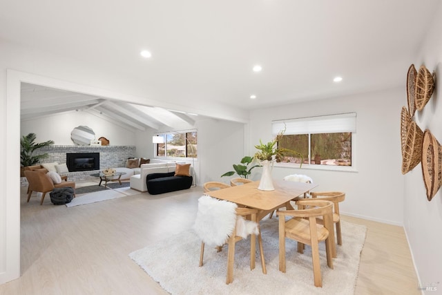 dining space featuring a fireplace, lofted ceiling with beams, and light wood-type flooring