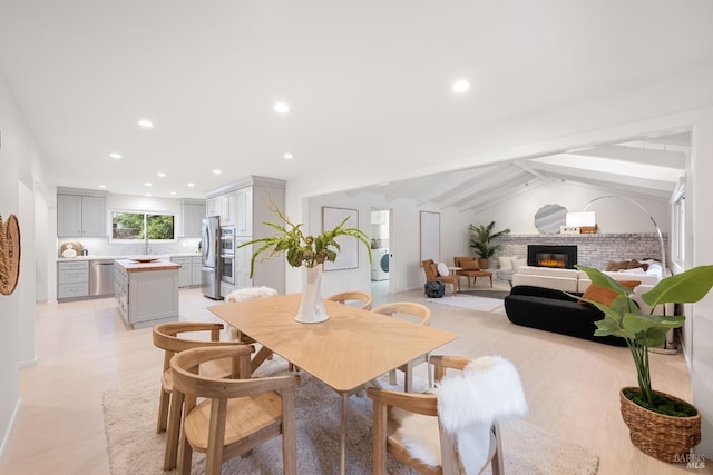 dining room featuring lofted ceiling with beams, a brick fireplace, and light hardwood / wood-style flooring