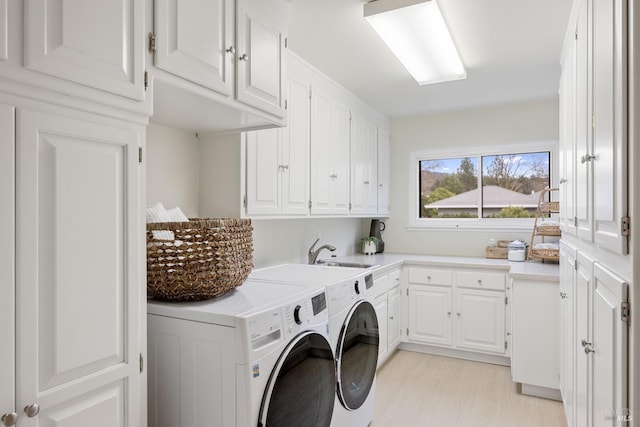 clothes washing area featuring separate washer and dryer, sink, light hardwood / wood-style floors, and cabinets