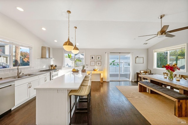 kitchen with stainless steel dishwasher, lofted ceiling, wall chimney exhaust hood, and gas range