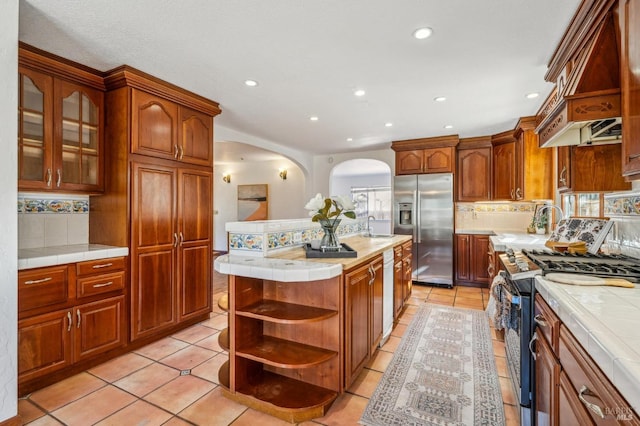 kitchen with a kitchen island, tile countertops, sink, stainless steel appliances, and custom range hood