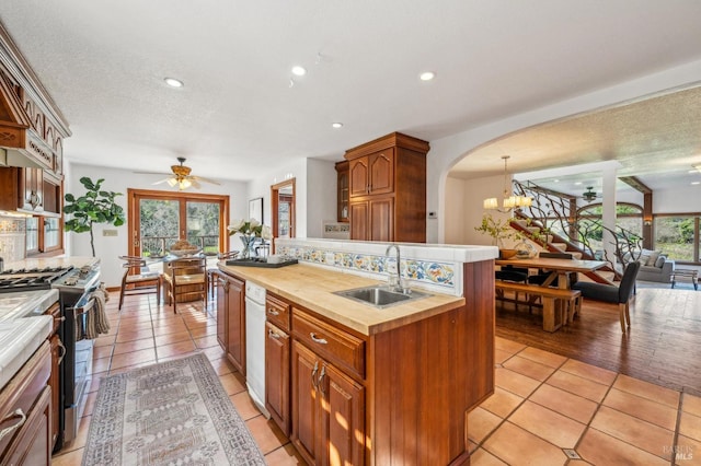 kitchen featuring light tile patterned flooring, stainless steel range with gas stovetop, sink, and a center island with sink