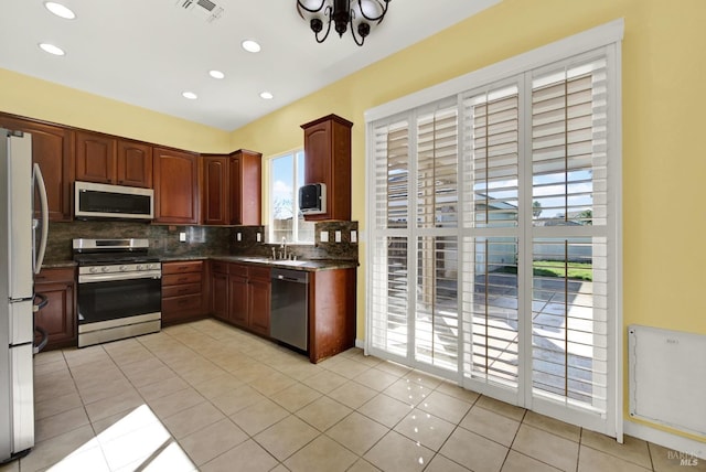 kitchen with stainless steel appliances, backsplash, light tile patterned floors, sink, and dark stone countertops