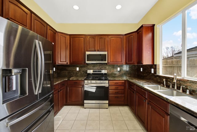 kitchen featuring dark stone countertops, light tile patterned floors, sink, stainless steel appliances, and decorative backsplash