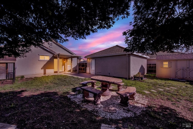 back house at dusk with a patio and a yard