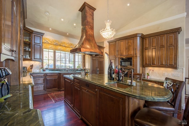 kitchen featuring lofted ceiling, a breakfast bar, decorative light fixtures, an island with sink, and island exhaust hood