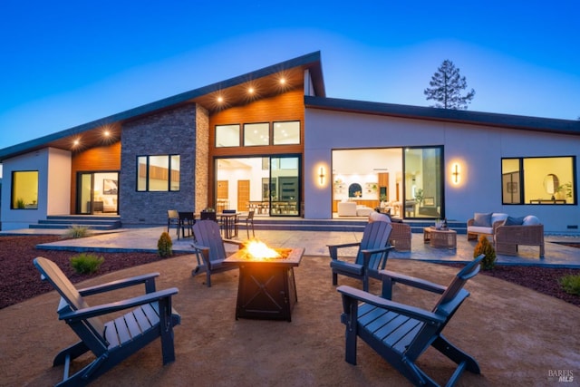 back of property with a patio, stone siding, an outdoor living space with a fire pit, and stucco siding