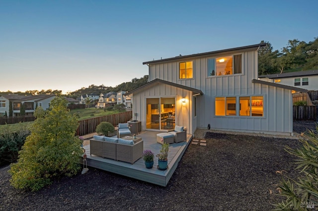 back of property at dusk featuring a residential view, fence, outdoor lounge area, and board and batten siding