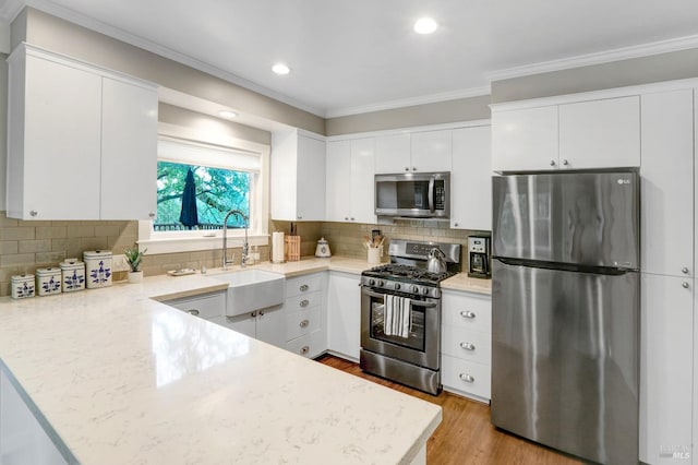 kitchen with a sink, stainless steel appliances, white cabinetry, a peninsula, and ornamental molding