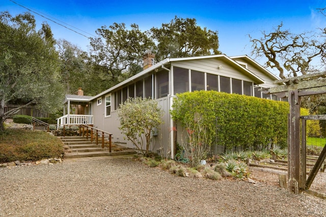 view of side of home featuring a sunroom, a chimney, and stairway