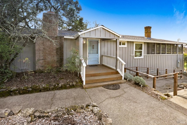 view of front of property featuring a sunroom, a chimney, board and batten siding, and roof with shingles