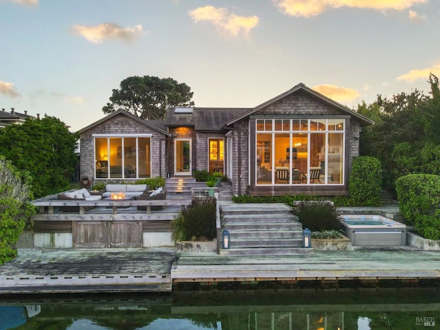 back house at dusk with a deck, outdoor lounge area, and an in ground hot tub