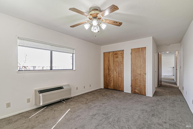 unfurnished bedroom with light carpet, ceiling fan, a wall unit AC, and two closets