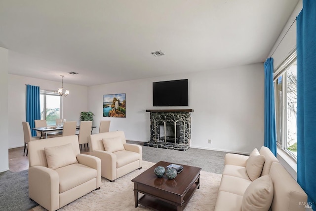 carpeted living room featuring a stone fireplace and a chandelier