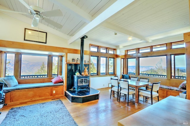 interior space with lofted ceiling with beams, a wood stove, ceiling fan, light hardwood / wood-style floors, and a mountain view