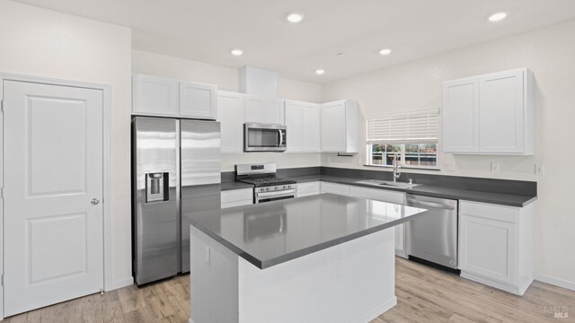 kitchen featuring appliances with stainless steel finishes, dark countertops, light wood-type flooring, a sink, and white cabinets