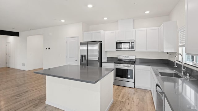 kitchen with dark countertops, light wood-type flooring, white cabinets, a sink, and stainless steel appliances
