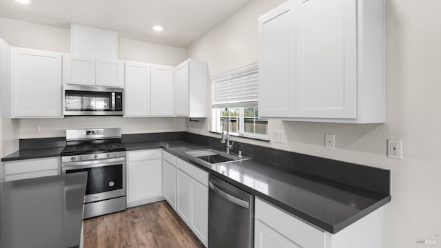 kitchen featuring appliances with stainless steel finishes, dark countertops, a sink, and white cabinetry