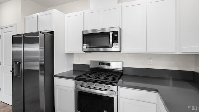 kitchen with dark countertops, appliances with stainless steel finishes, white cabinetry, and wood finished floors