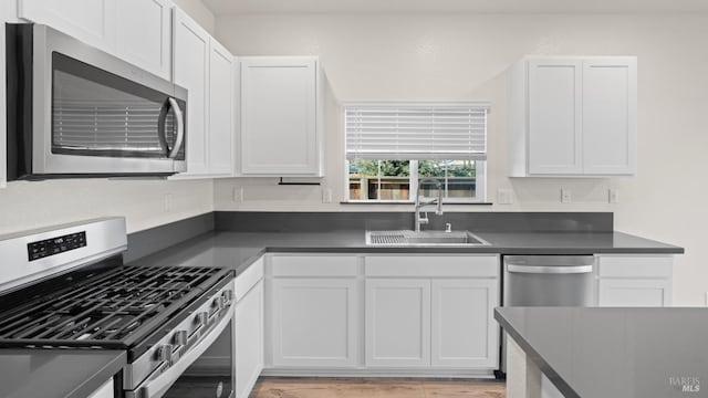 kitchen with stainless steel appliances, dark countertops, white cabinetry, and a sink