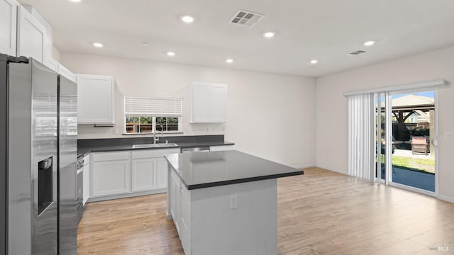 kitchen featuring light wood-style flooring, stainless steel appliances, a sink, visible vents, and dark countertops