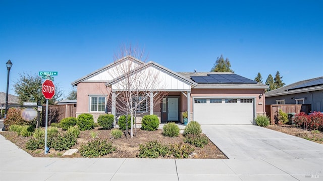 craftsman inspired home with an attached garage, fence, concrete driveway, roof mounted solar panels, and stucco siding