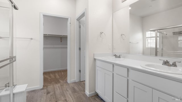 bathroom featuring double vanity, a spacious closet, a sink, and wood finished floors
