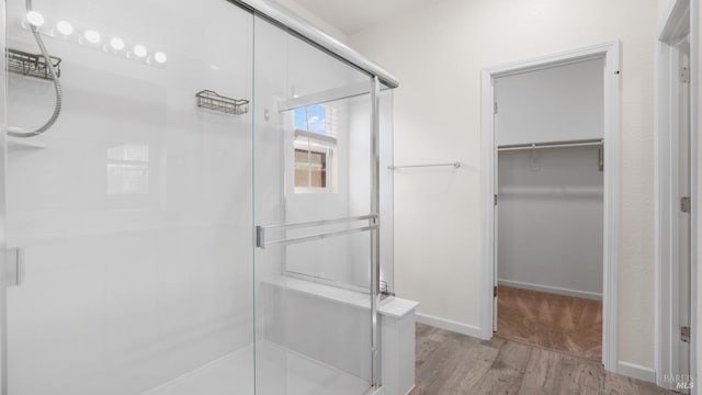 full bathroom featuring a stall shower, a spacious closet, and wood finished floors