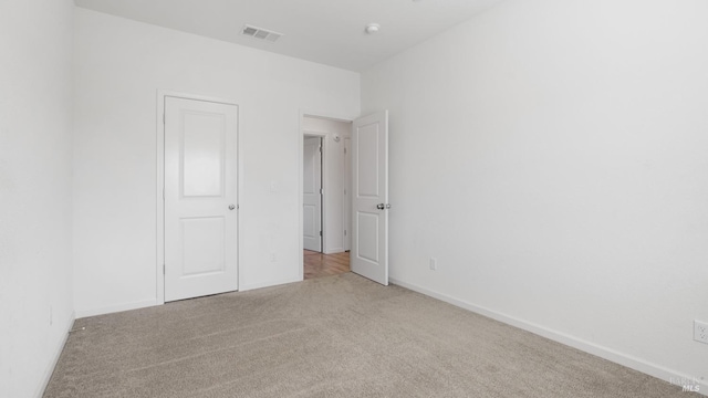 unfurnished bedroom featuring baseboards, light colored carpet, and visible vents