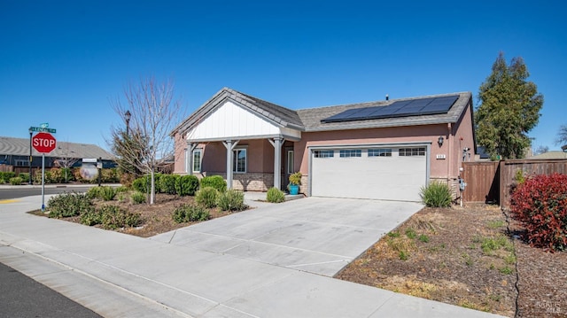 view of front of house with a porch, a garage, driveway, roof mounted solar panels, and stucco siding