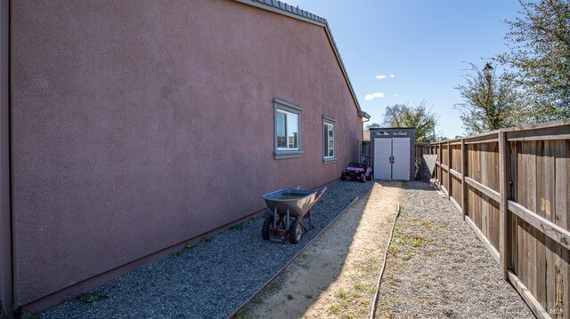 view of side of property with a fenced backyard, an outdoor structure, stucco siding, and a shed