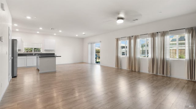 unfurnished living room with recessed lighting, light wood-style floors, ceiling fan, a sink, and baseboards