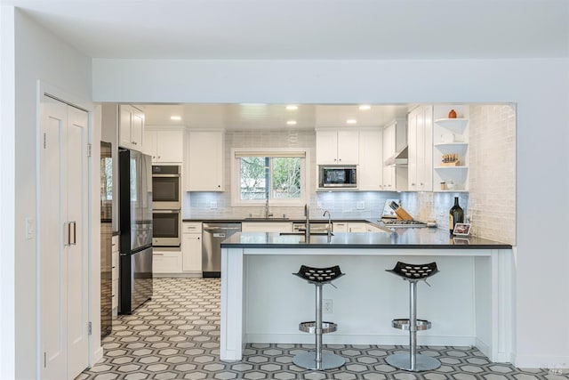 kitchen featuring under cabinet range hood, stainless steel appliances, a peninsula, a sink, and dark countertops