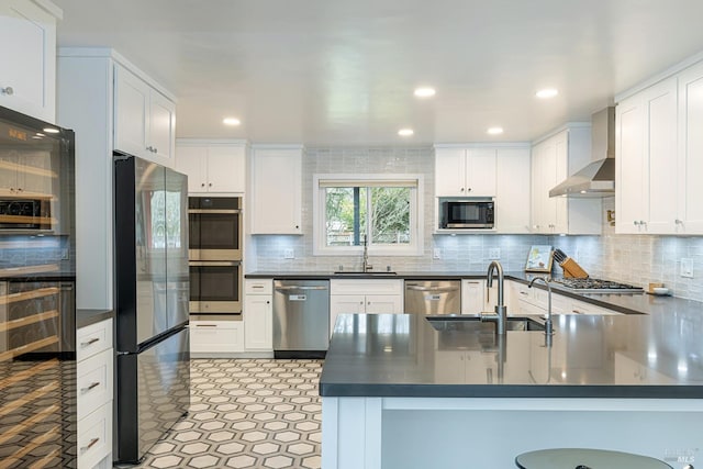 kitchen featuring dark countertops, wall chimney range hood, stainless steel appliances, and a sink