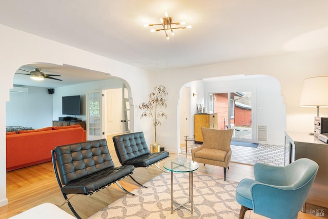 living room with light wood-style floors, arched walkways, a wall unit AC, and ceiling fan with notable chandelier