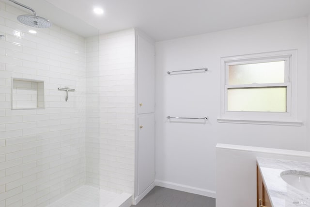 full bathroom with tile patterned flooring, a tile shower, vanity, and baseboards