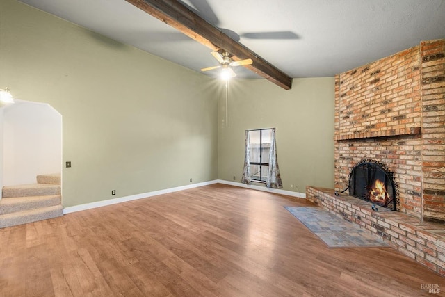 unfurnished living room featuring a brick fireplace, beam ceiling, wood-type flooring, and ceiling fan