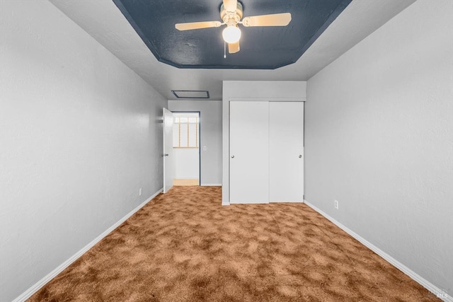 unfurnished bedroom with ceiling fan, light colored carpet, a tray ceiling, and a closet