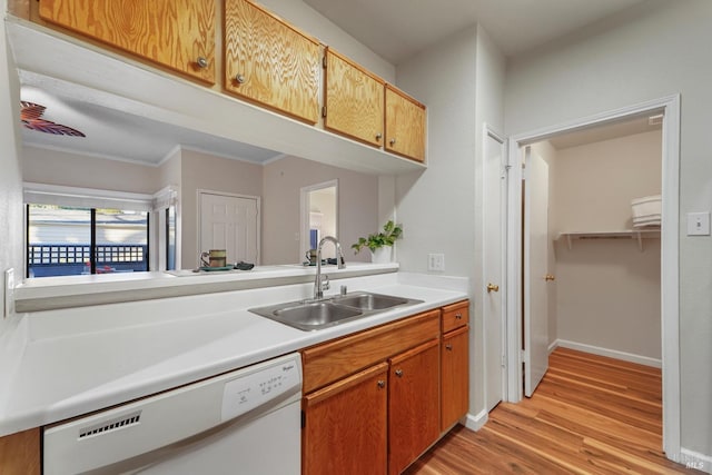 kitchen with white dishwasher, a sink, baseboards, light countertops, and light wood finished floors