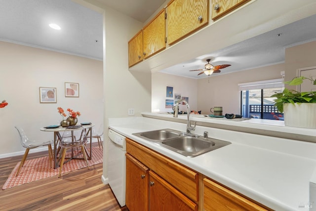 kitchen featuring light countertops, light wood-style flooring, ornamental molding, a sink, and dishwasher