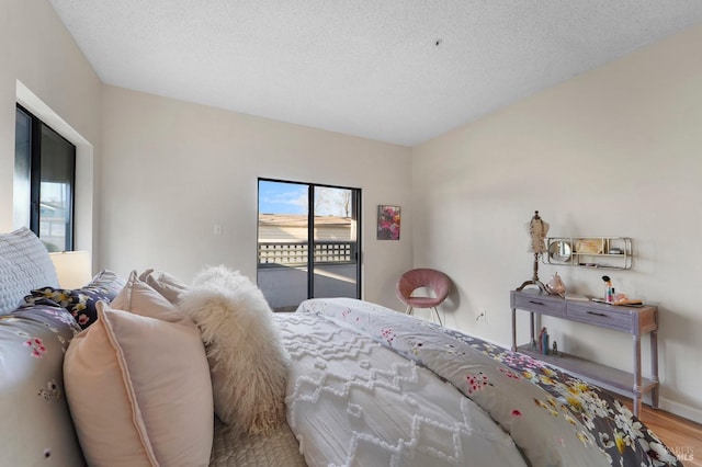 bedroom with a textured ceiling, access to outside, wood finished floors, and baseboards