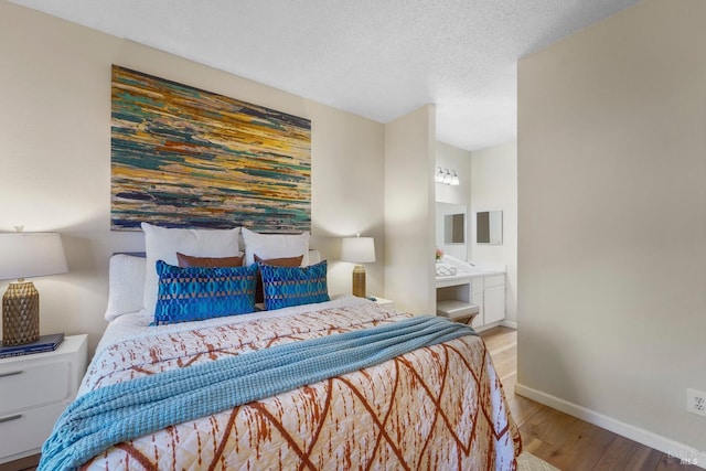 bedroom with a textured ceiling, baseboards, wood finished floors, and ensuite bathroom