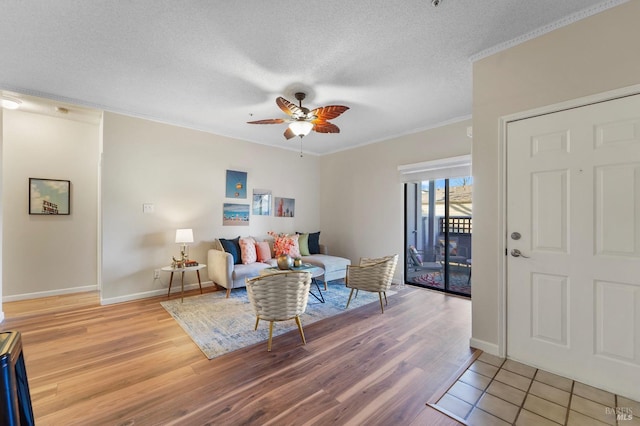 living room featuring crown molding, light wood-style floors, a ceiling fan, a textured ceiling, and baseboards