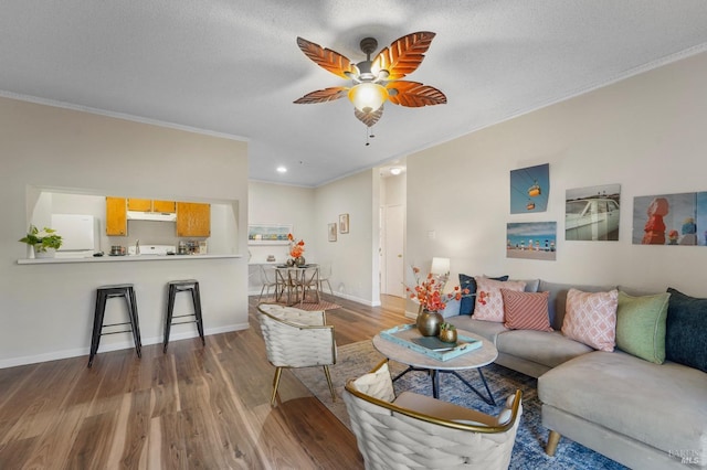 living area with ornamental molding, a ceiling fan, a textured ceiling, wood finished floors, and baseboards