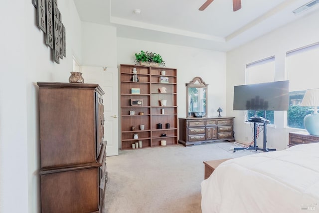 bedroom with ceiling fan, light colored carpet, and a tray ceiling