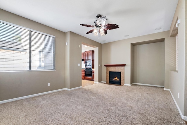 unfurnished living room with ceiling fan, a tile fireplace, and light colored carpet